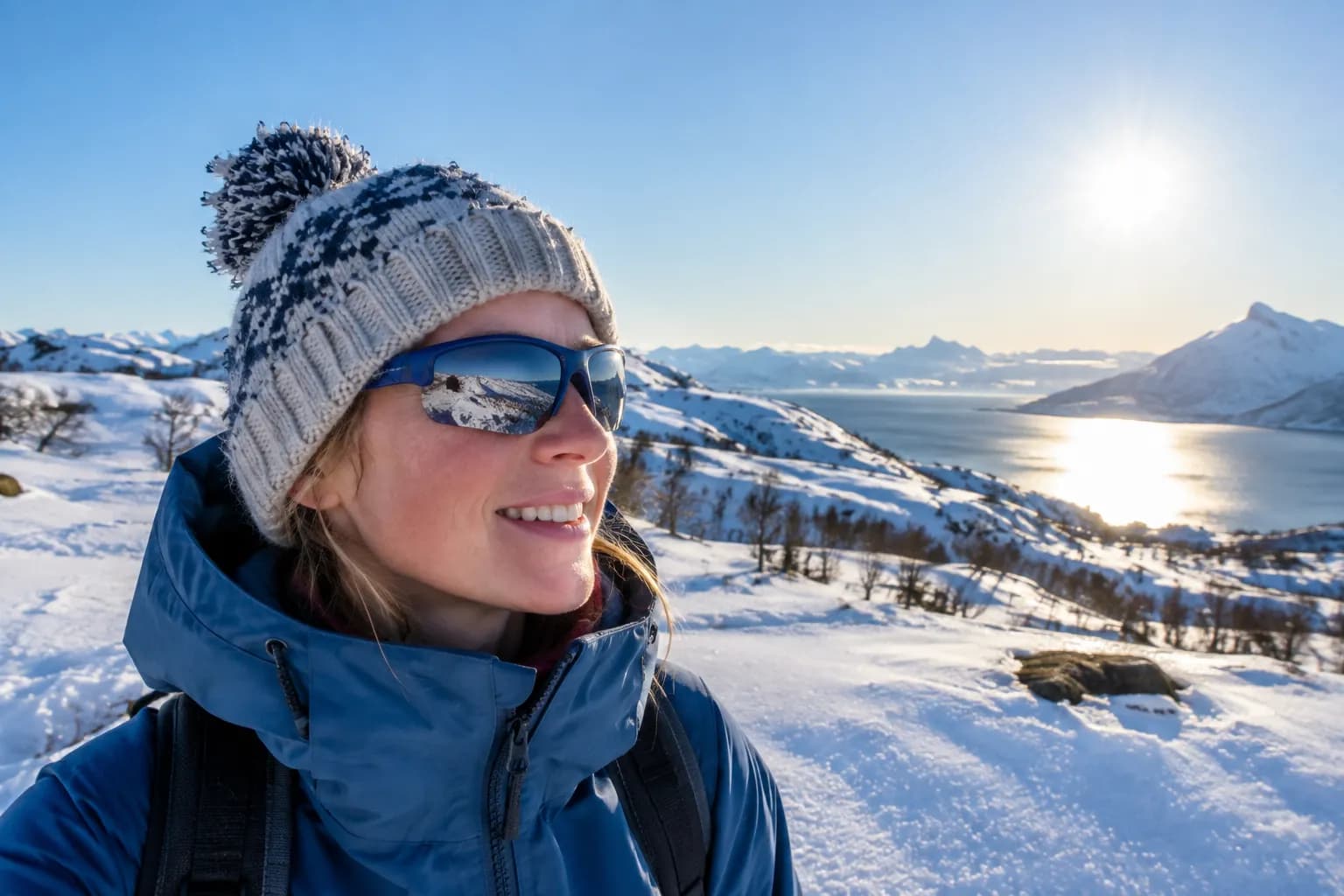 Person med sportslige solbriller og lue i et solfylt snølandskap med lav vintersol